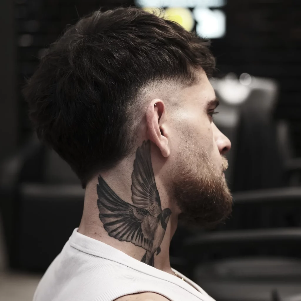 Coupe dégradée sur cheveux foncés et barbe avec tatouage de colombe visible